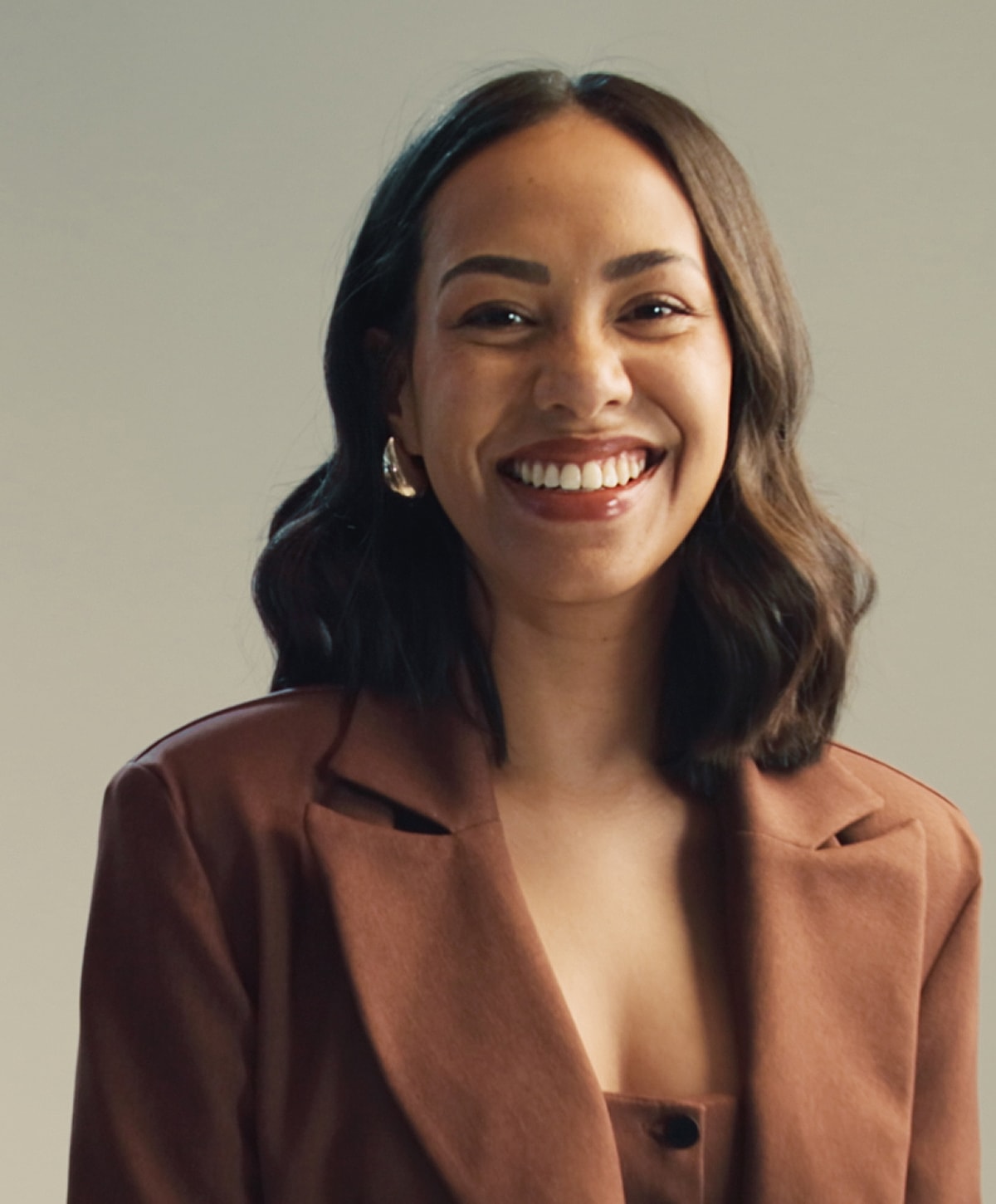 Smiling Melbourne facial implant model in a brown blazer background.