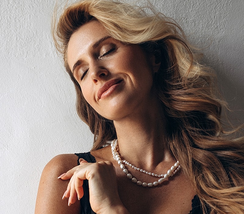 Melbourne facial cosmetic surgery model smiling with pearl necklace against wall.