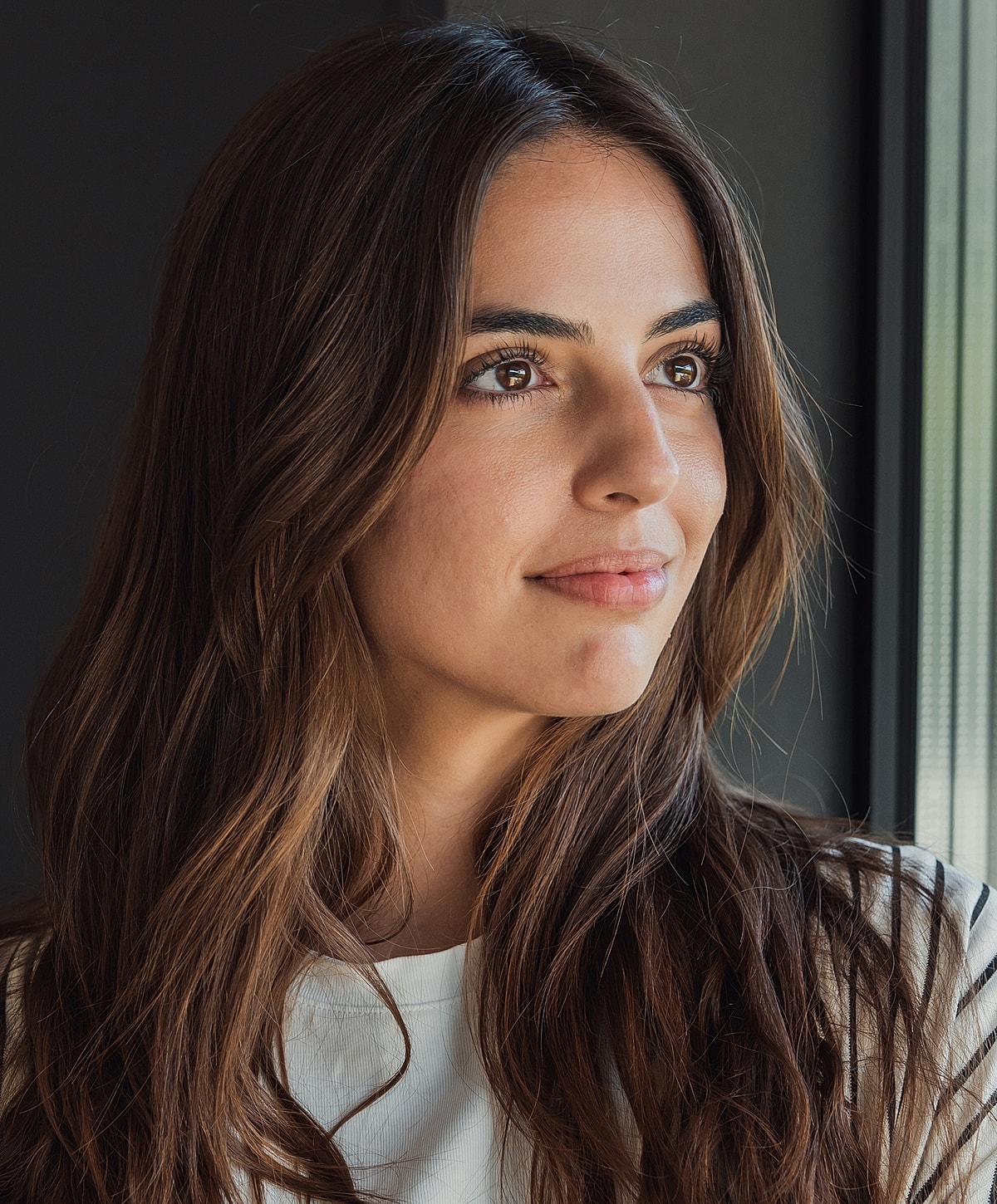 Woman with long brown hair, thoughtful expression.