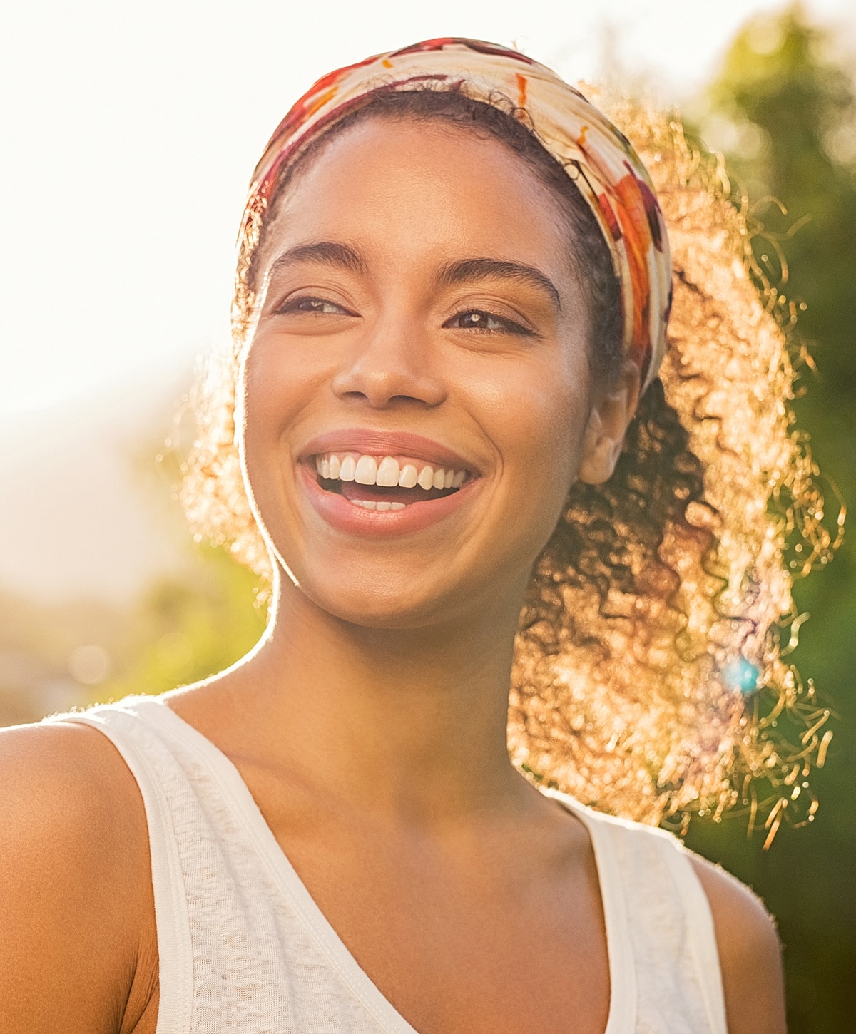 Smiling Melbourne microneedling model with curly hair in sunlight.