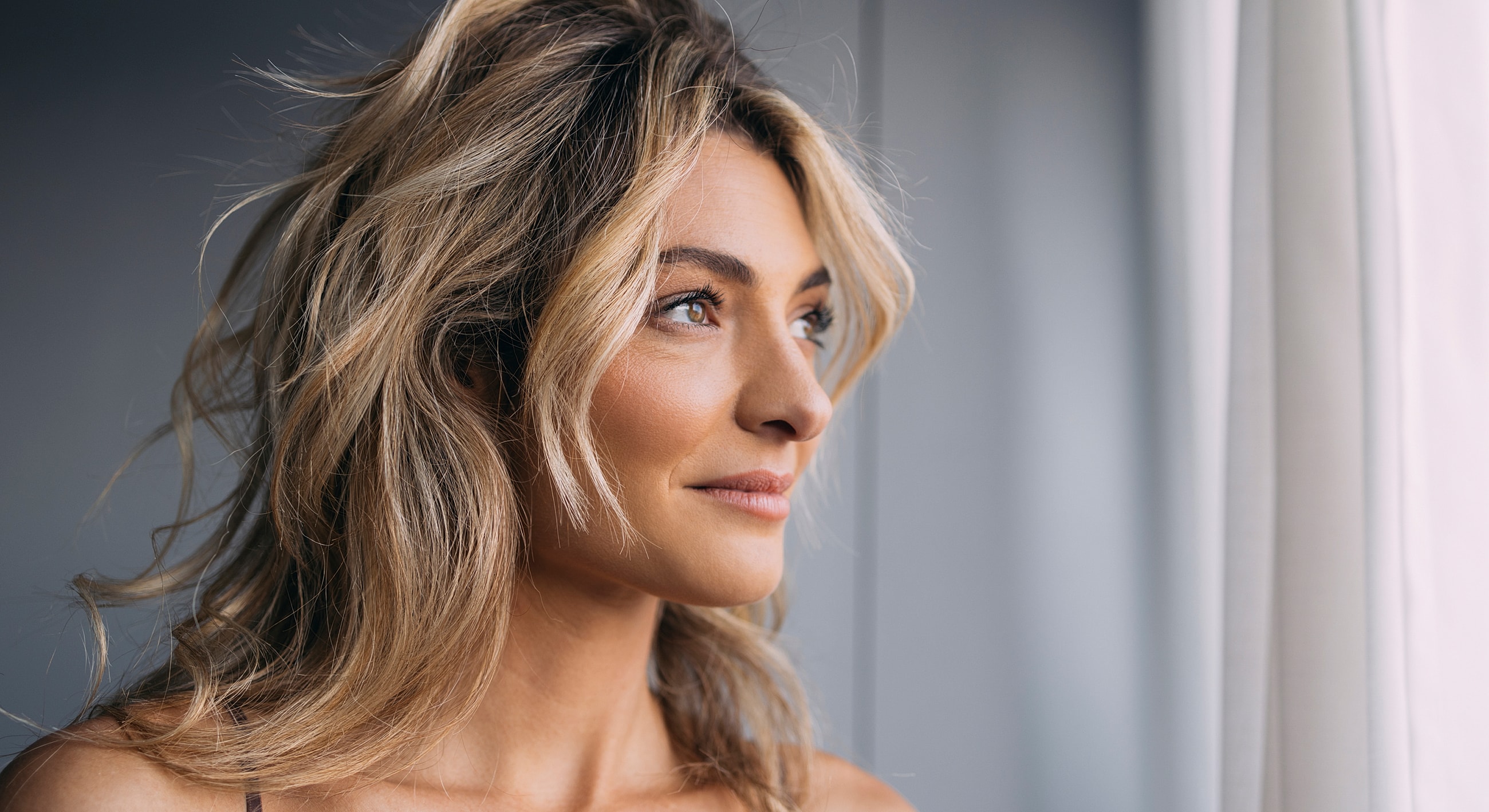 Woman gazing out a window with light background.