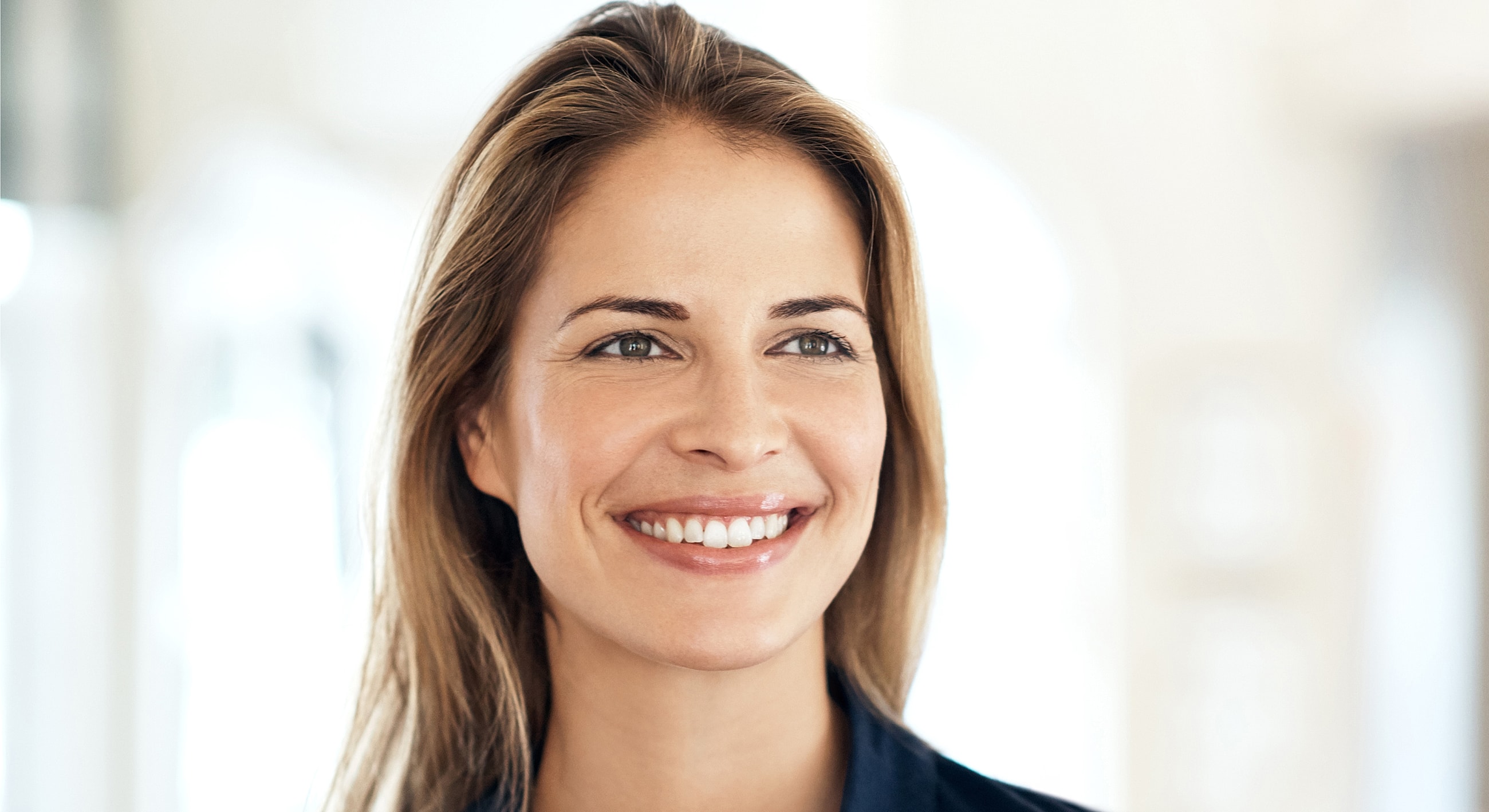 Smiling woman with long hair in bright setting.