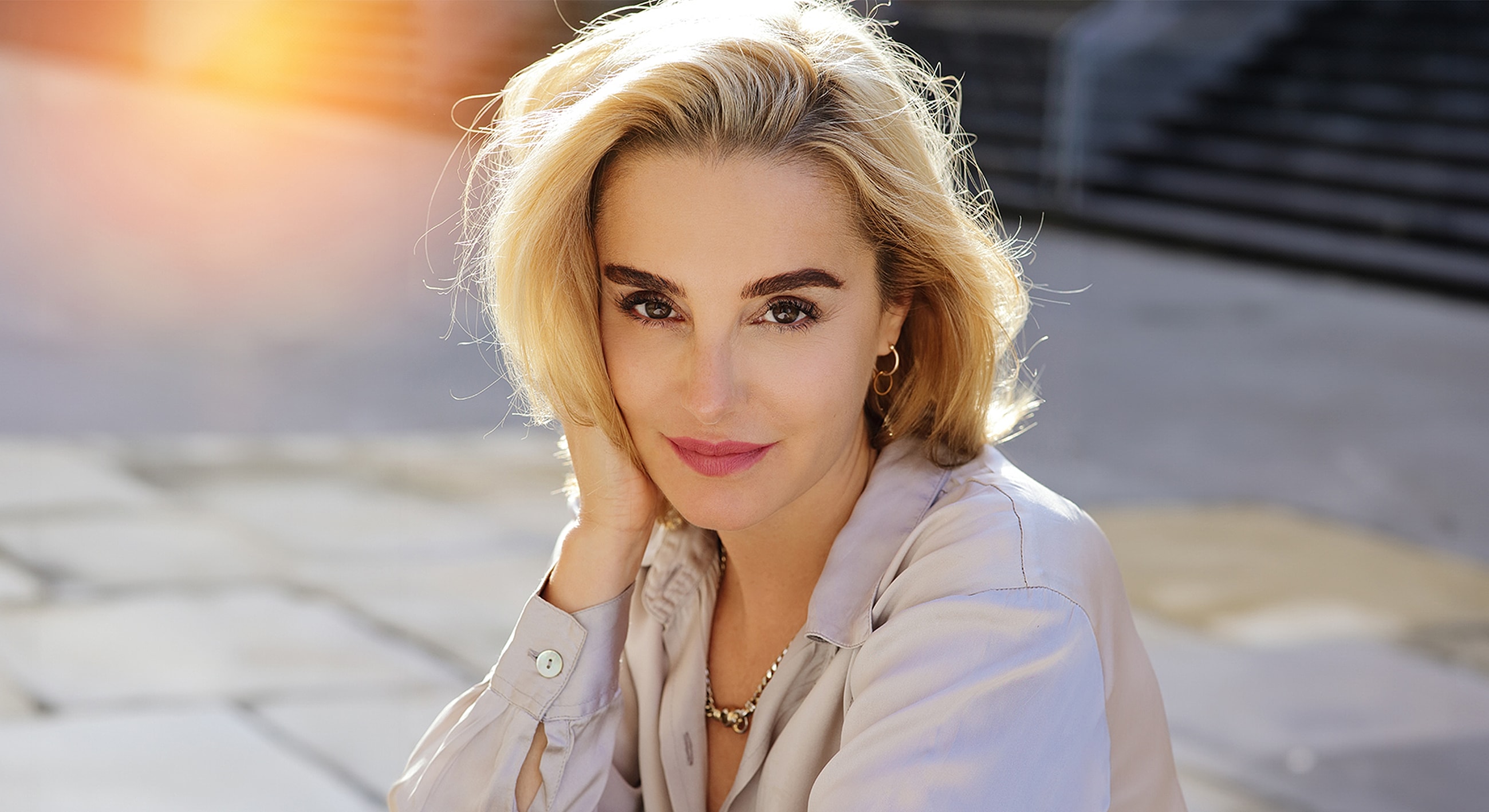 Smiling woman with blonde hair outdoors in sunlight.