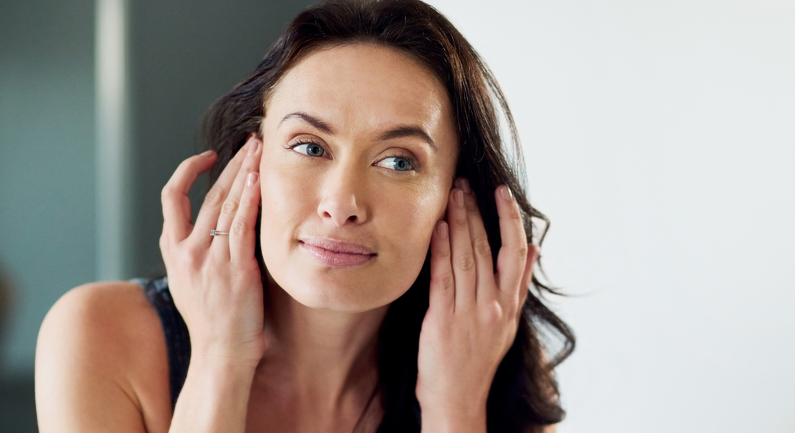 Woman applying skincare in front of a mirror.